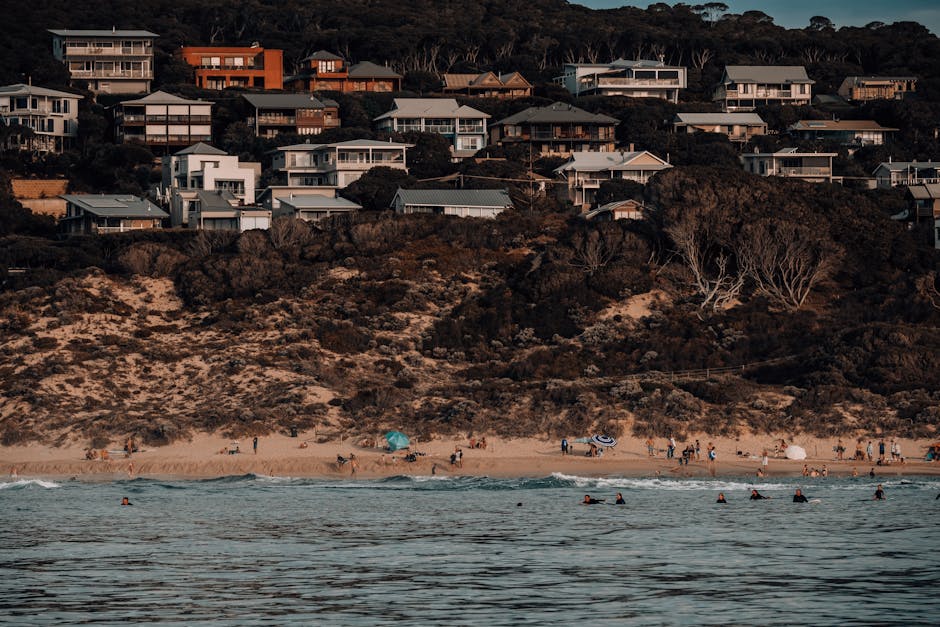 A picturesque scene with beachfront houses, tourists enjoying the beach, and tranquil ocean waves