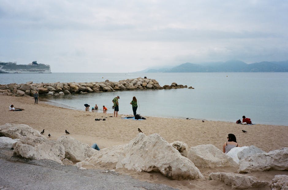 Back view of unrecognizable group of travelers on sandy ocean coast with stones behind mountains under cloudy sky